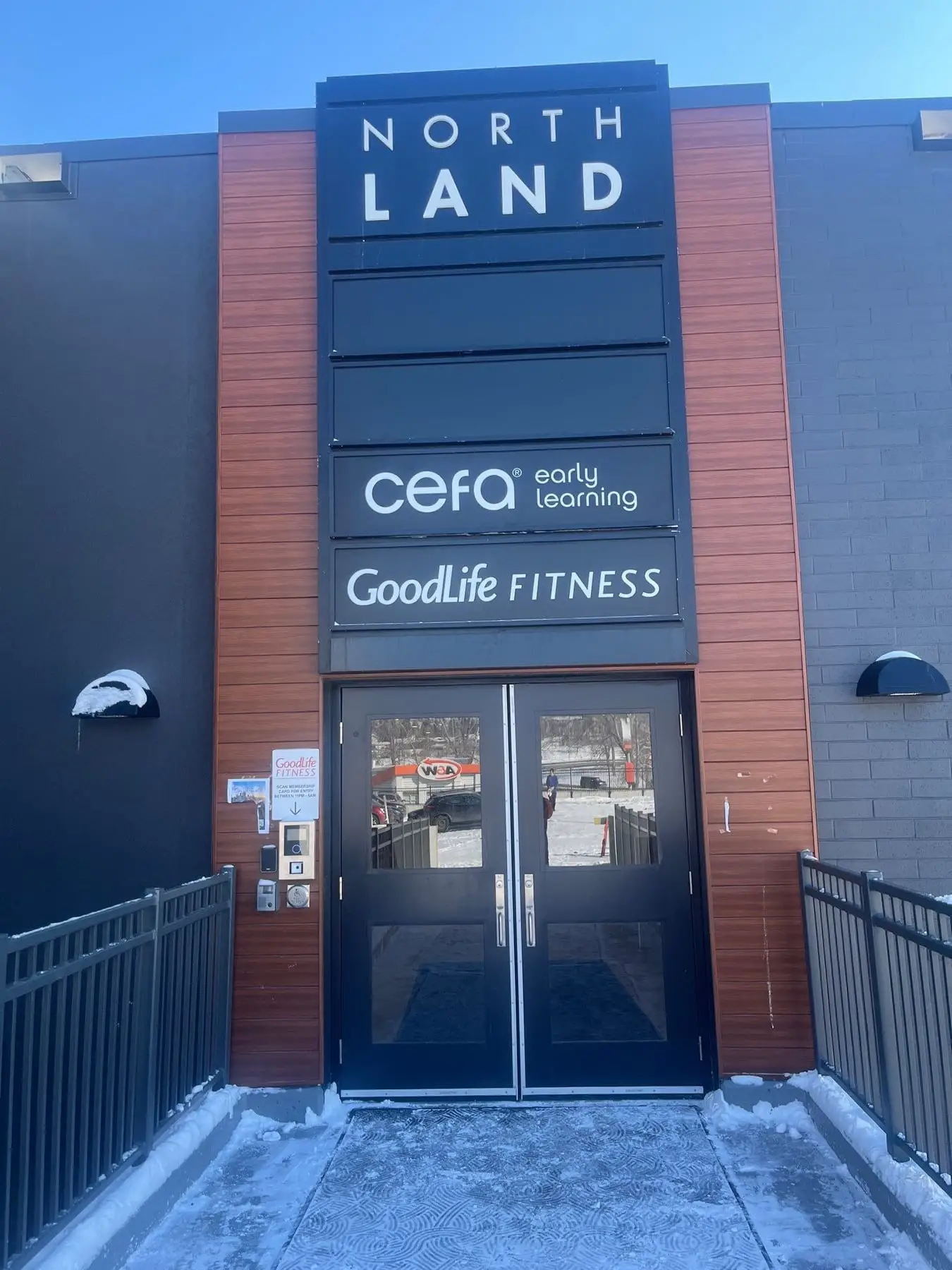 Three separate tenant signs stacked on one building elevation above a glass entrance in Calgary