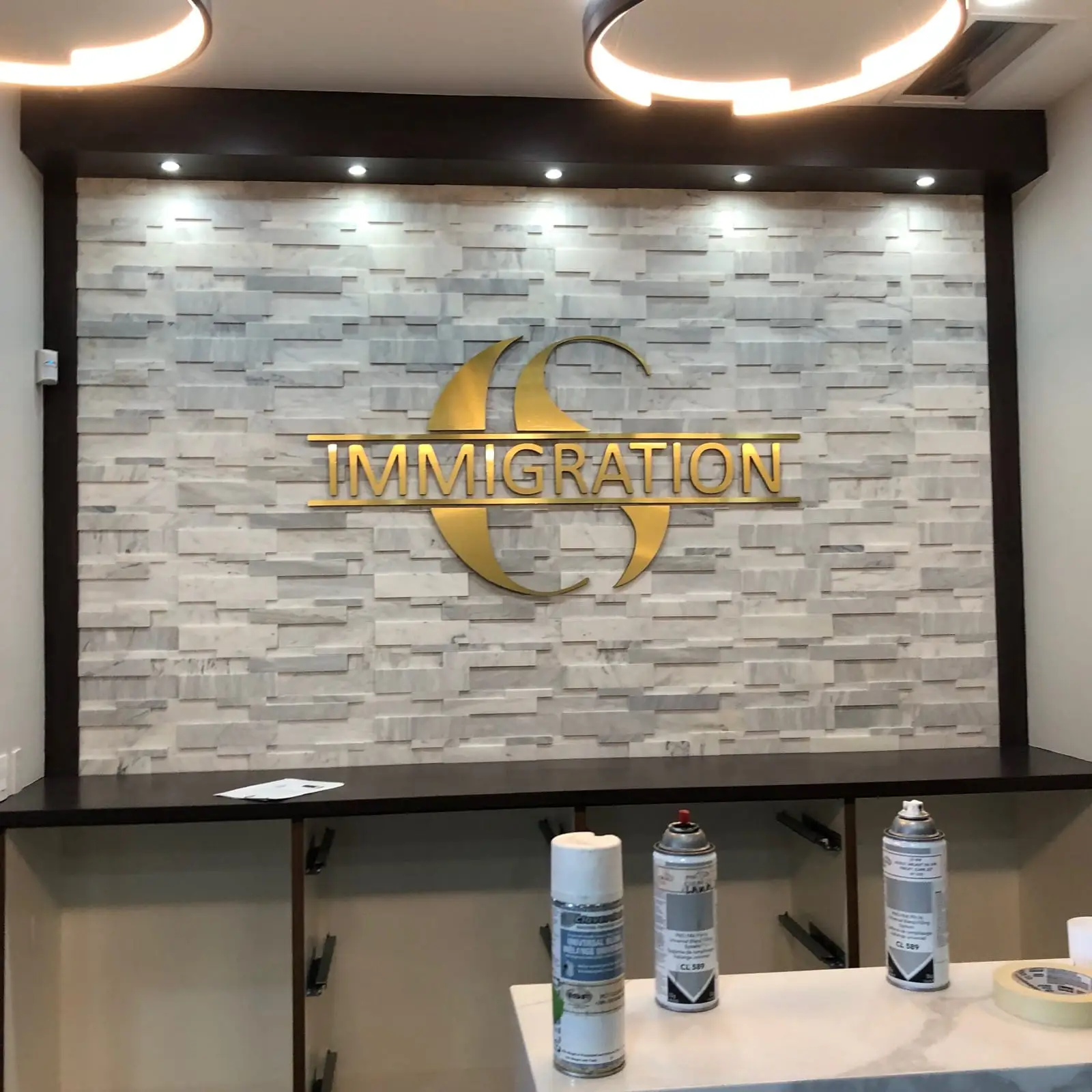 Brushed gold dimensional lettering mounted on a stone feature wall behind a reception desk