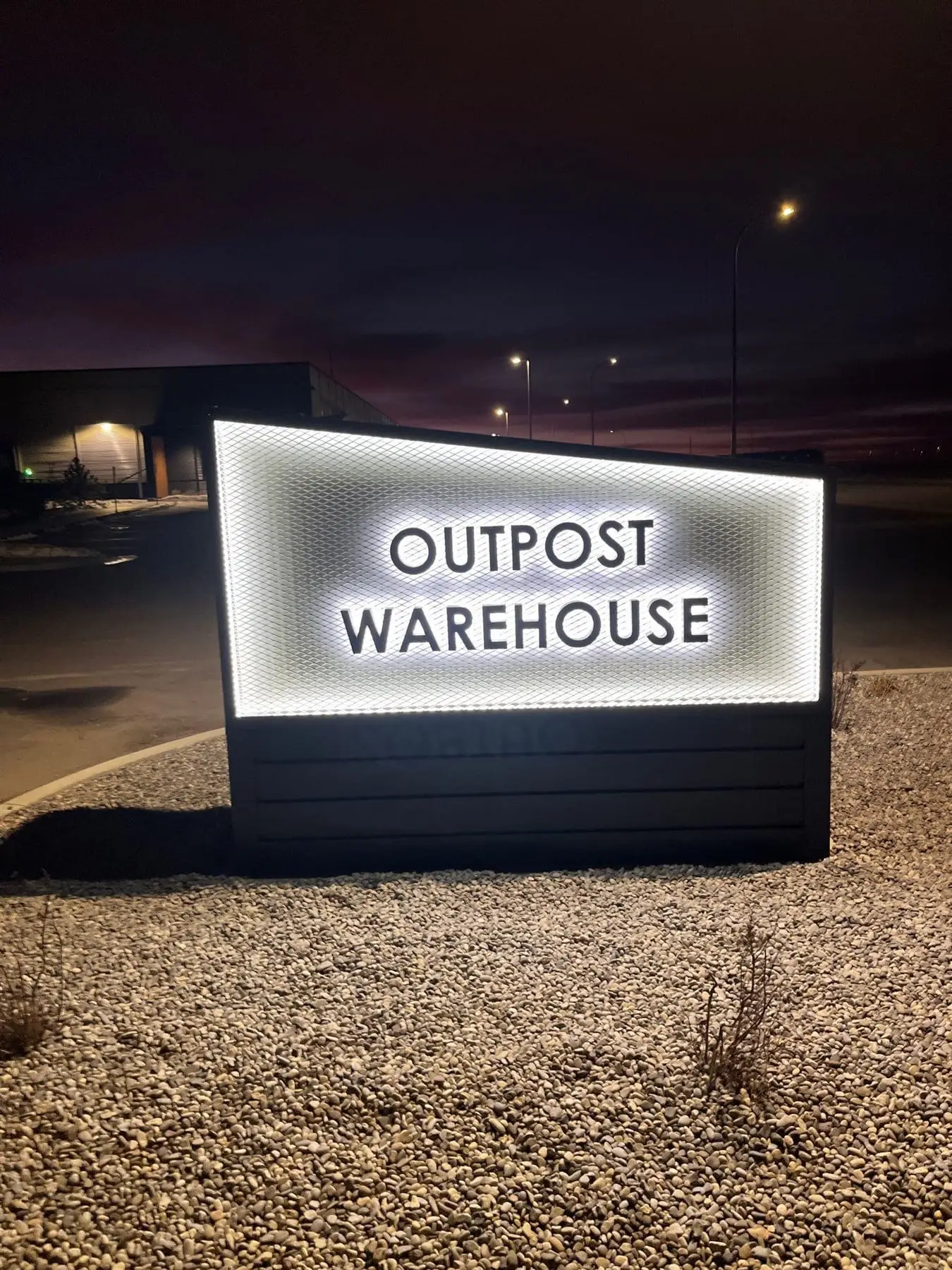 An internally illuminated monument sign glowing white at night outside a Calgary warehouse