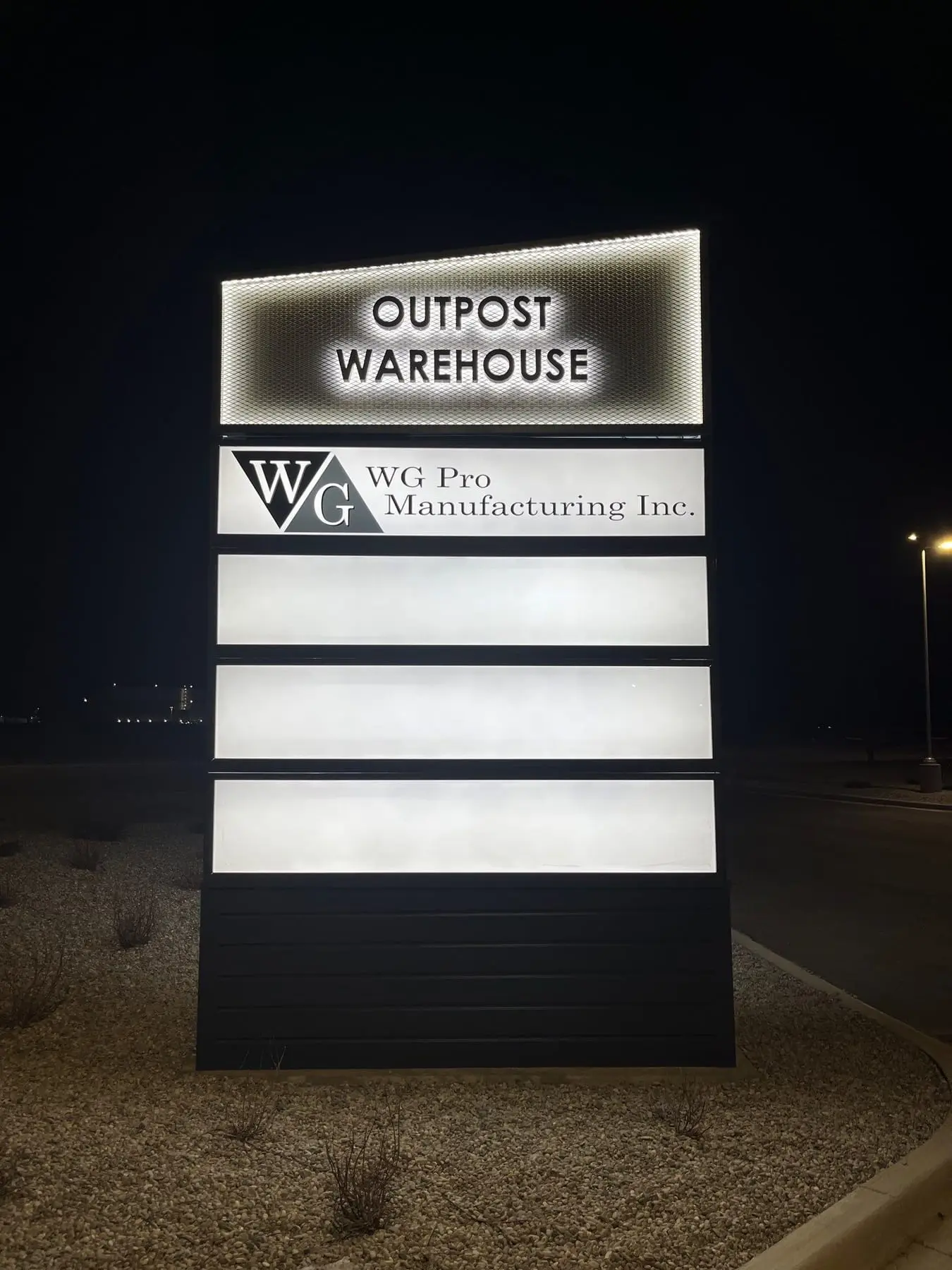 An illuminated pylon sign glowing at night outside a Calgary manufacturing and warehouse site