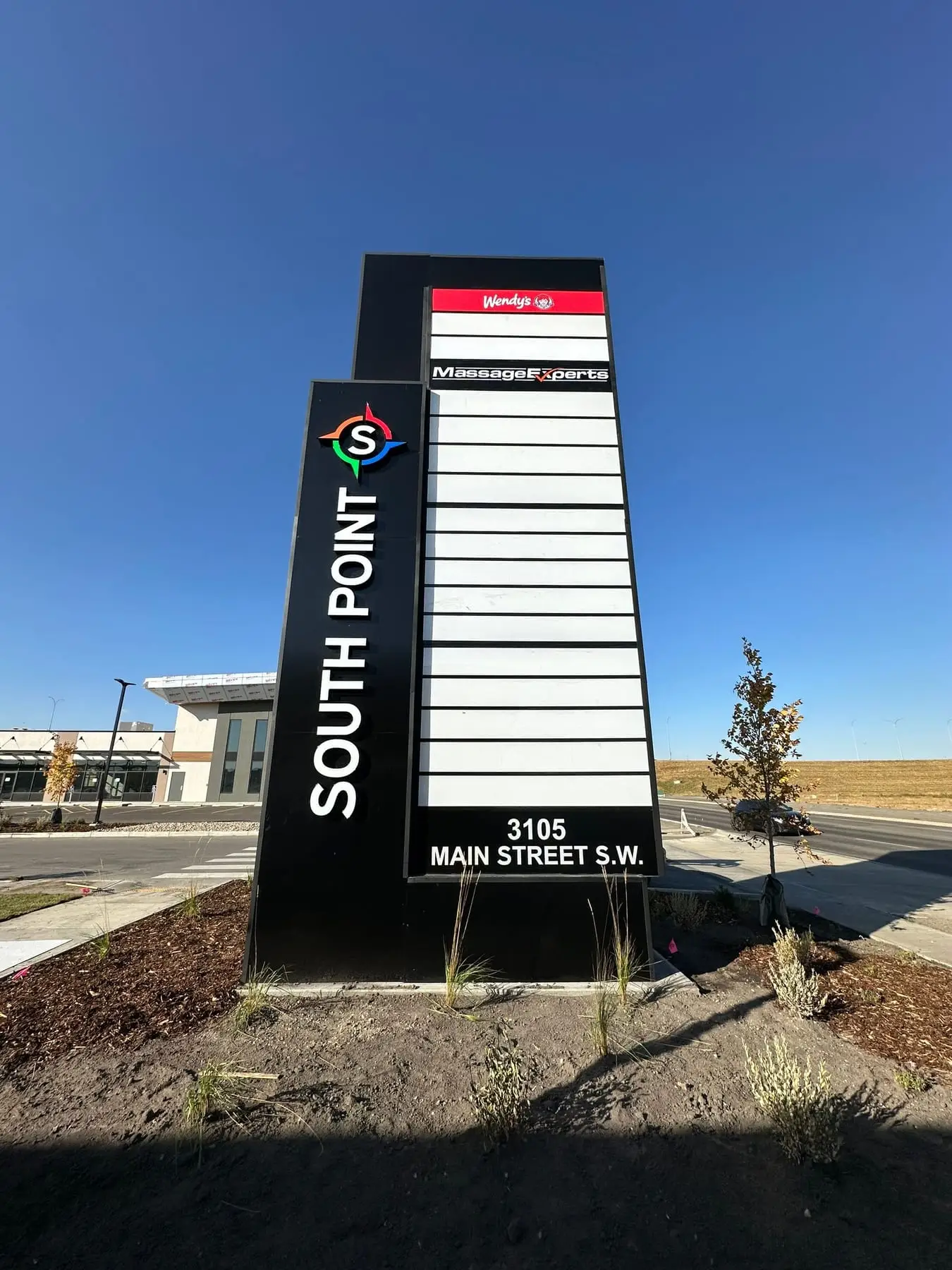 A finished multi-tenant pylon sign standing on its base at a Calgary retail site, with the tenant panels and address panel installed